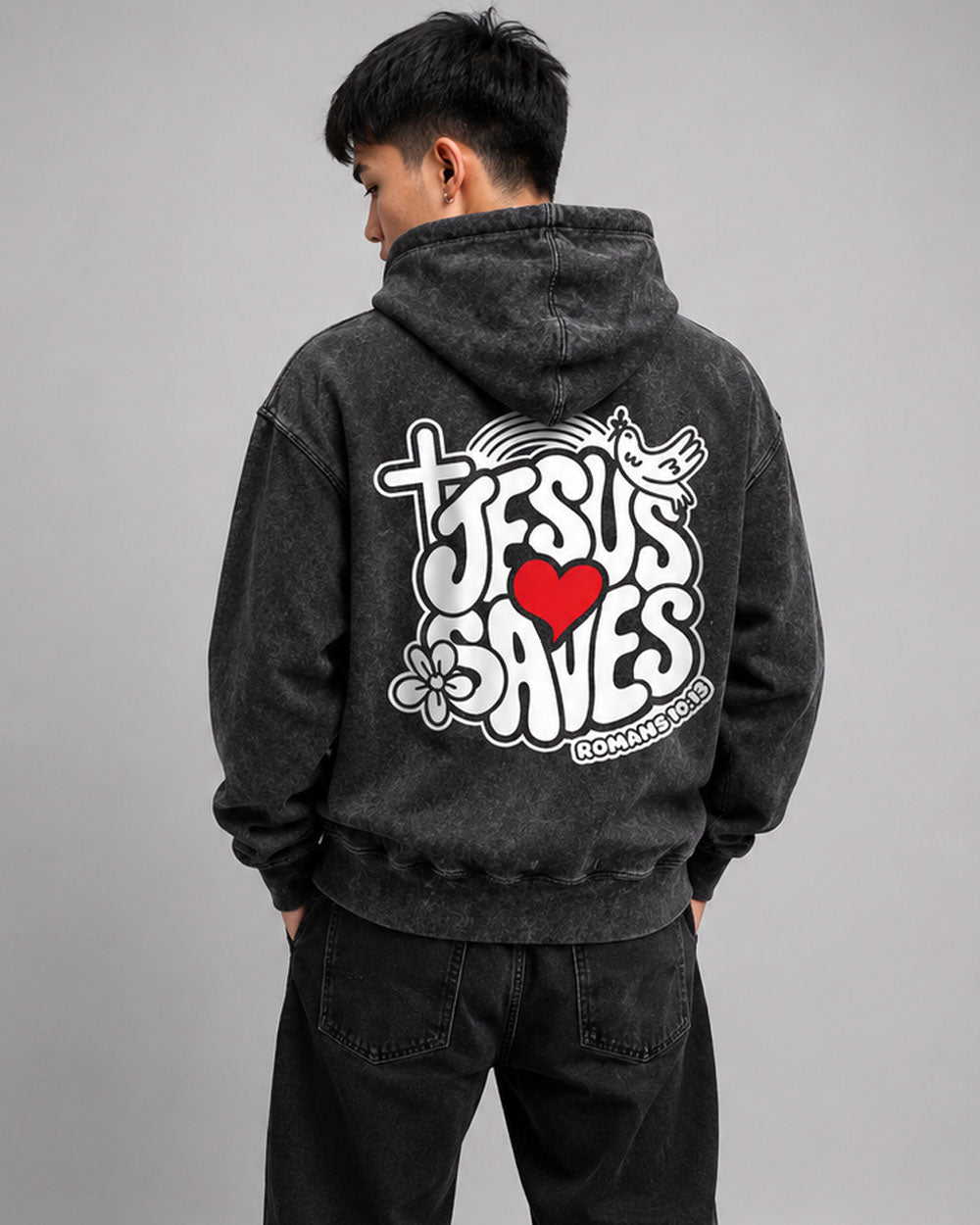 An african american man showing the back of a black hoodie with a grafitti style lettering of the words King Jesus, with a crown on the end of the letter S on a concrete background.