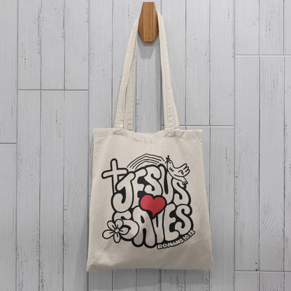 Tote bag with 'Jesus Saves' design hanging on a wooden hook against a light wooden panel background